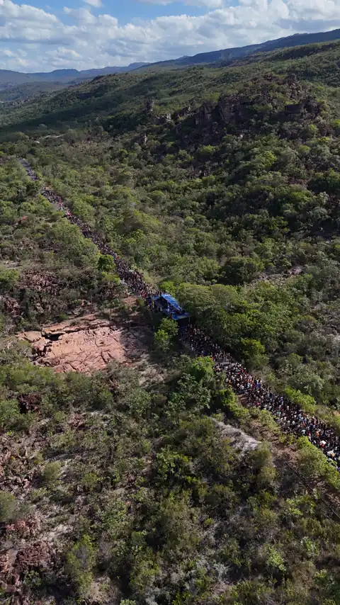 Vista aérea da multidão subindo a estrada, com as serras e o céu ao fundo